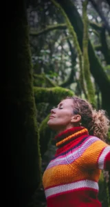 Mujer con los brazos abiertos y los ojos cerrados en medio del bosque, conectando con la naturaleza y su mundo interior.