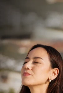Mujer con los ojos cerrados y la cabeza inclinada, respirando profundamente en un momento de calma y conexión interior.