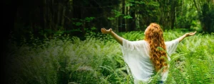 Mujer de espaldas con los brazos abiertos y la cabeza inclinada hacia atrás, conectando con la naturaleza.