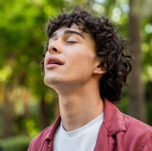 Hombre con los ojos cerrados respirando profundamente en un entorno natural, en conexión con su interior.