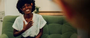 Mujer sonriente con la mano sobre el pecho durante una sesión de psicoterapia uno a uno, mientras escucha a su terapeuta.